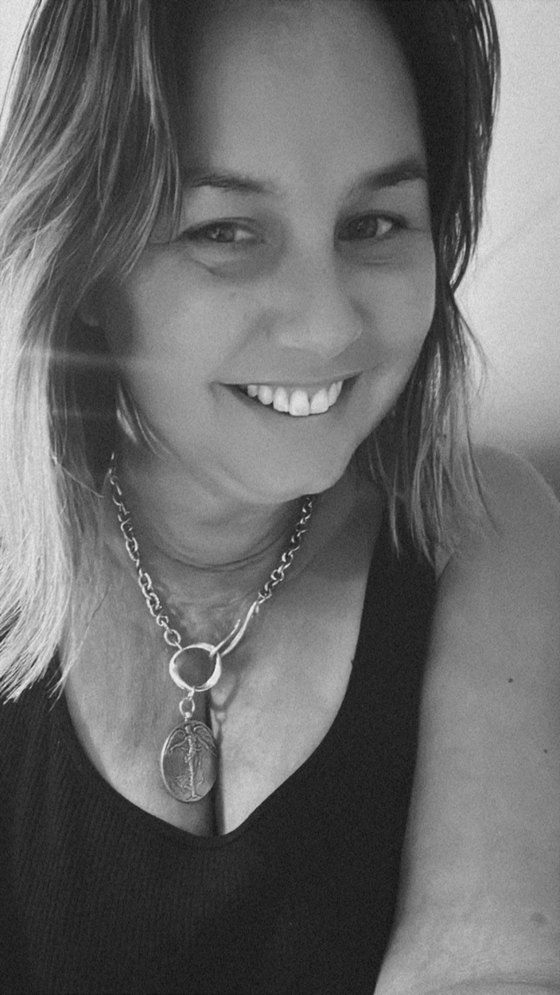 Black and white photo of Mandy smiling, head tilted, wearing a silver pendant necklace